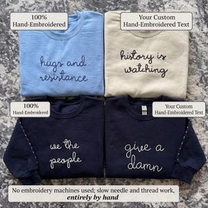 May include: Four crewneck sweatshirts in light blue, beige, and navy blue. Each sweatshirt features hand-embroidered text: "hugs and resistance", "history is watching", "we the people", and "give a damn". The text "100% Hand-Embroidered" is also visible.