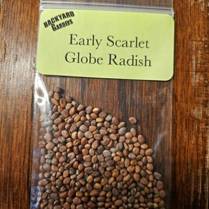 May include: A small clear plastic bag filled with brown radish seeds. The bag has a yellow label that reads "Backyard Gardens" and "Early Scarlet Globe Radish".