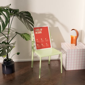 May include: A green chair with a red poster that says "Laws of Design" hanging on the back of it. A white lamp with an orange base is on a white and pink tiled table.