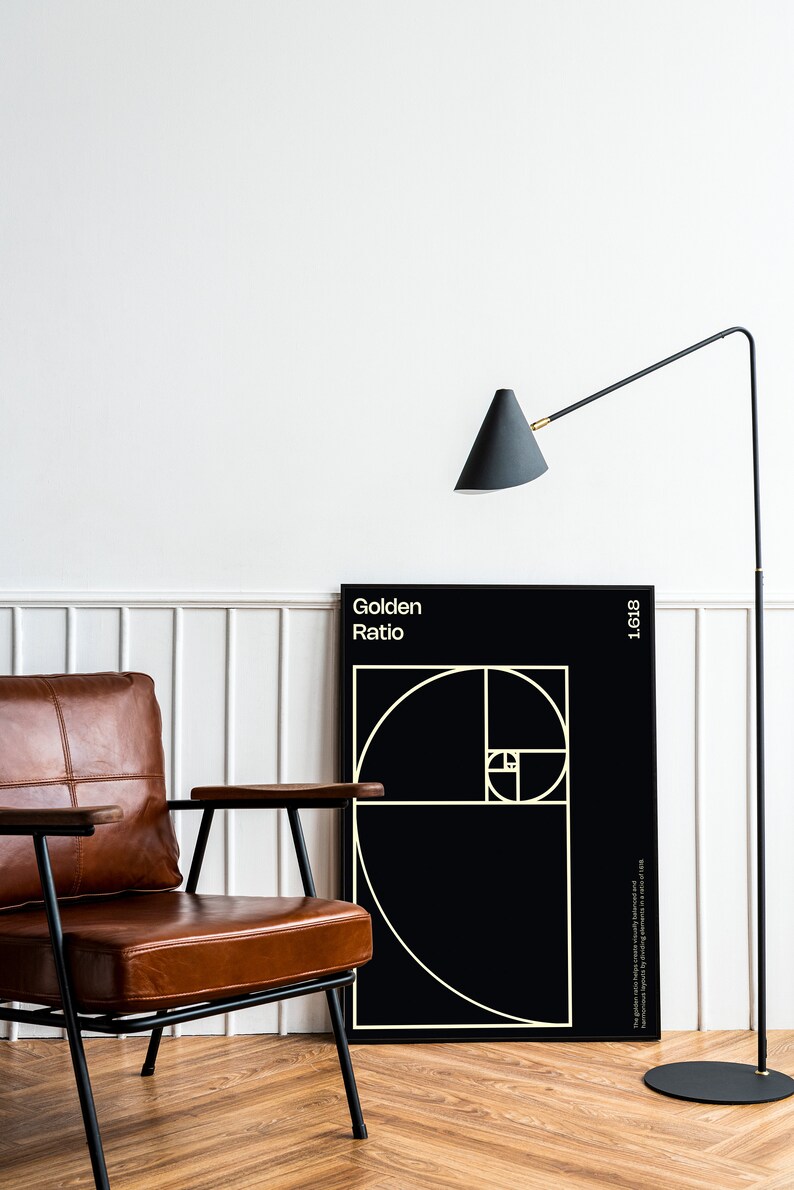 May include: A black and white poster with the text "Golden Ratio" and a geometric design of overlapping circles. The poster is hanging on a white wall next to a brown leather armchair and a black floor lamp.