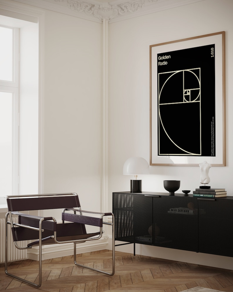 May include: A black and white poster with the text "Golden Ratio" and a geometric design in gold. The poster is framed in a light wood frame and hanging on a white wall. A black cabinet with a grid pattern is in the foreground.