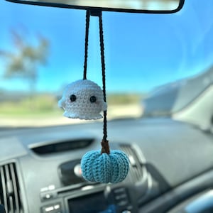 May include: A white crocheted ghost and a blue crocheted pumpkin hanging from a rearview mirror in a car.