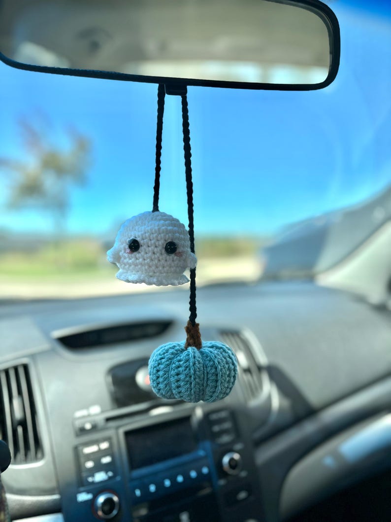 May include: A white crocheted ghost and a blue crocheted pumpkin hanging from a rearview mirror in a car.
