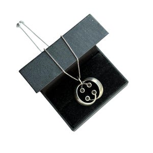 May include: A silver necklace with a circular pendant featuring a black onyx stone and a silver design. The necklace is in a black velvet box.