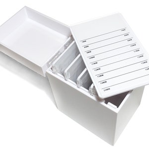 Op de afbeelding: Witte plastic opbergdoos met een transparant deksel. Het deksel heeft een label met afmetingen in millimeters van 7 mm tot 15 mm. De doos is ontworpen om wimperextensions in op te bergen.