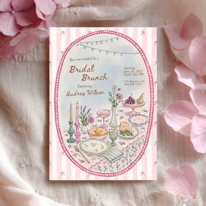 May include: A rectangular invitation card with a pink and white striped border featuring an oval illustration of a table set for a bridal brunch. The text reads: You are invited to a Bridal Brunch honoring Audrey Wilson, Sunday June 20, 2027, 3:00 PM, 123 Anywhere St, Any City 12345.