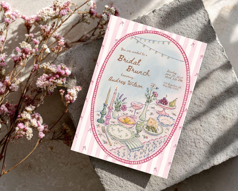 May include: A rectangular invitation card featuring a pink and white striped border with small bow illustrations. The center oval graphic depicts a table setting with candles, flowers, fruit, and plates, with text reading Bridal Brunch honoring Audrey Wilson.