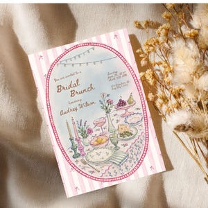 May include: A rectangular invitation card with a pink and white striped border featuring a central oval illustration of a table set for a bridal brunch. The text reads: You are invited to a Bridal Brunch honoring Audrey Wilson, Sunday June 28, 2027, start 3:00 PM, 123 Anywhere St., Any City 12345.