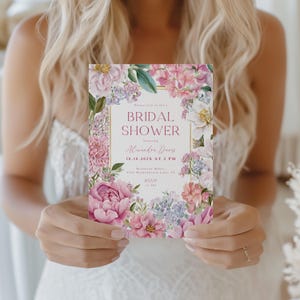 Op de afbeelding: Een bloemen uitnodiging voor een bruidsdouche met een gouden rand, met roze en paarse bloemen. De uitnodiging bevat de tekst "Bridal Shower" en evenementdetails. De kaart wordt door een persoon vastgehouden.