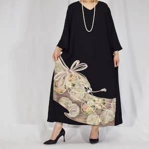 以下が含まれることがあります： Vネックの黒いドレスで、ゆったりとした袖と長く流れるようなシルエットが特徴です。下部にはライトブラウンの背景に装飾パネルがあり、大きなクリーム色のスタイリッシュなリボンと円形のフローラルパターンが施されています。