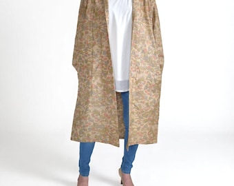 May include: A long, open-front coat with a floral pattern in beige, green, and pink. The coat is worn over a white top and blue jeans. The coat has a relaxed fit and falls to the ankles.