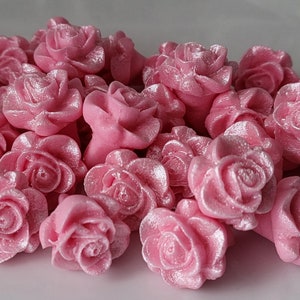 May include: A collection of pink rose-shaped decorations. The roses have a glossy finish and a subtle shimmer. These decorative flowers are ideal for crafts, cake decorating, or other creative projects.