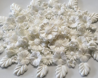 Può includere: Un assortimento di decorazioni floreali e a forma di foglie bianche perlate. La collezione comprende vari tipi di fiori, come rose e margherite, insieme a forme di foglie dettagliate. Alcuni fiori hanno una piccola perla al centro. Decorazioni per torte o artigianato.