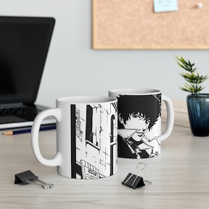 Puede incluir: Dos tazas de cerámica blanca con ilustraciones en blanco y negro. Una taza presenta un personaje del anime Cowboy Bebop, mientras que la otra taza presenta una ciudad.