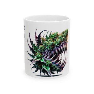 Puede incluir: Una taza de cerámica blanca con una ilustración gráfica de una criatura monstruosa compuesta por cogollos y hojas de cannabis verdes con dientes afilados y puntiagudos. El diseño muestra tonos vibrantes de verde, morado y colores oscuros.