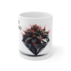 Puede incluir: Taza de cerámica blanca con un diseño de diamante negro y una ilustración de cogollo de cannabis. El cogollo tiene detalles en rojo y verde. Las palabras "Black Diamond" están impresas en la taza.