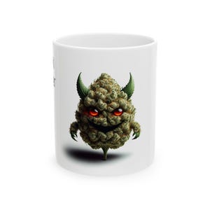 May include: A white ceramic mug featuring a central graphic of a green, textured, bud-like character with sharp horns, glowing red eyes, and a wide, mischievous grin. The character has small, claw-like appendages and a pointed base.