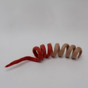 Op de afbeelding: Een spiraalvormige decoratie van gevilt wol met een kleurverloop van diep, verzadigd rood aan de linkerkant naar een zachte, gedempte beige kleur aan de rechterkant. Het object is gevormd in een doorlopende, spiraalachtige krul.