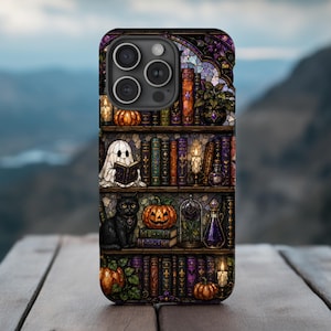 May include: A phone case featuring a stained glass design of three bookshelves filled with books, pumpkins, a ghost reading a book, a black cat, candles, and potion bottles in shades of purple, orange, green, and gold against a dark background.