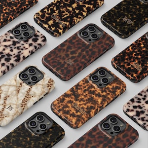 May include: A collection of phone cases with various animal print designs, including leopard and marble patterns. Some cases feature initials or names like "Sarah" and "Mila" in a stylish font. The cases have a glossy finish and a raised camera bump.