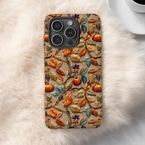 May include: A smartphone case featuring a repeating pattern of orange pumpkins, brown, yellow, and teal leaves, and small berries set against a light wood grain background. The case has a cutout for a triple-lens camera system on the top left.