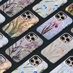 May include: A collection of iridescent phone cases with floral designs. The cases feature various iris and other flower patterns in shades of white, blue, purple, and green. The cases have a glossy finish and a dark background.