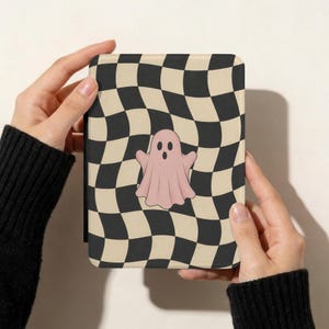 May include: A rectangular e-reader case featuring a wavy black and cream checkerboard pattern across the entire surface. Centered on the front of the case is a single, solid light pink ghost illustration with two black oval eyes and an open mouth.