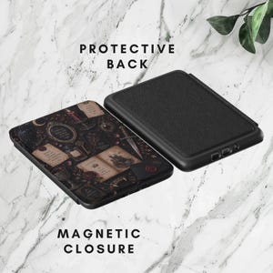 May include: A black e-reader case featuring a dark, intricate pattern of vintage mirrors, candles, keys, and open books on the front cover. The back of the case is solid black with a textured finish. The case includes a magnetic closure mechanism.