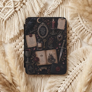 May include: A rectangular e-reader case featuring a dark, intricate illustration of a raven, a crescent moon, a burning candle, a dagger, a goblet, and an open book with a castle drawing. Text includes "I would burn the world for you" and "Beware for I am fearless and therefore powerful."