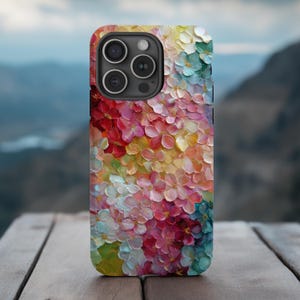 May include: A colorful phone case featuring a floral design with a textured, impasto effect. The case showcases a vibrant array of colors, including red, pink, yellow, and blue, creating a painterly aesthetic. The phone case is on a wooden surface.
