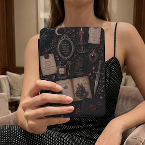 May include: A black e-reader case featuring a dark, gothic-inspired collage of a raven, a burning candle, a dagger, an open book with a castle illustration, a perfume bottle, a key, and parchment notes with text including I WOULD BURN THE WORLD FOR YOU.