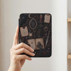 May include: A rectangular e-reader case featuring a dark, gothic-inspired print with a raven, a lit candle, a dagger, an open book with a castle illustration, a wax-sealed envelope, and various text snippets including "I would burn the world for you."