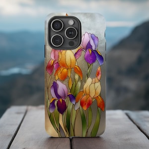 May include: A smartphone case featuring a colorful floral design of irises. The flowers are depicted in shades of purple, orange, and yellow with green stems against a gold background. The case has a glossy finish and a black border.