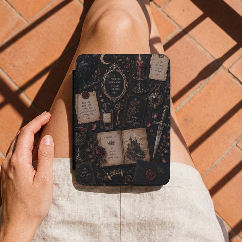 May include: A black e-reader case featuring a dark, gothic-inspired pattern with illustrations of a candle, a dagger, an open book with a castle, a potion bottle, a key, and various text snippets including "I would burn the world for you."