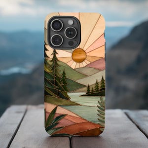 May include: A phone case featuring a stained glass style landscape illustration. The design depicts a sun rising over rolling hills, a calm lake, and evergreen trees in shades of green, brown, peach, and cream with dark outlines.