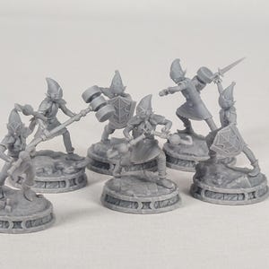 Könnte beinhalten: Eine Sammlung grauer Miniatur-Fantasy-Figuren, jede in einer aktiven Pose. Die Figuren stehen auf dekorativen Sockeln und scheinen Elfen oder ähnlichen Charakteren zu ähneln, einige mit Waffen wie Hämmern und Schwertern. Das Thema deutet auf ein Tabletop-Spiel oder Sammlerobjekt hin.