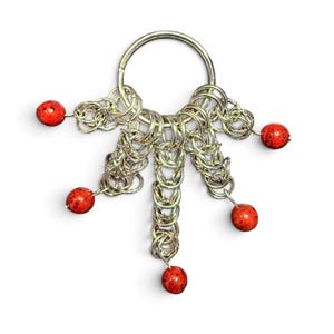 May include: A silver-toned metal keychain featuring a circular ring connected to five dangling chainmaille segments. Each of the five segments terminates in a single, round, speckled red bead, creating a fan-like arrangement of metallic links.
