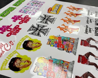 May include: A sheet of stickers with various designs, including a red and white "Storm and Grace" logo, a black and white "Storm and Grace" logo, a yellow and green "Storm and Grace" logo, a black and white cross with "Storm and Grace" text, a red and white "Next Up" logo, a red and white "Hood Hop" logo, a red and white "W2XH W2XH W2XH" logo, a red and white "Barrio" logo, and a red and white basketball player logo.