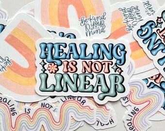 May include: A stack of colorful rainbow stickers with the text "Healing is not linear" in blue and teal lettering. The stickers are on a white background.