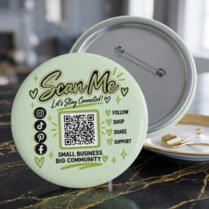 May include: A round, light green pin-back button featuring the text Scan Me, Let's Stay Connected!, and Small Business Big Community. It includes a central QR code, social media icons for Instagram, TikTok, Pinterest, and Facebook, and text labels for Follow, Shop, Share, and Support, decorated with small heart and star graphics.