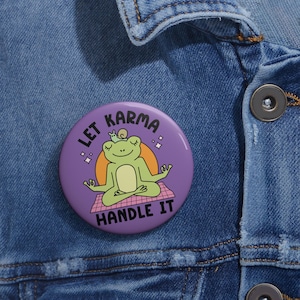 May include: Purple button with a green frog meditating with a snail on its head. The button says "Let Karma Handle It".