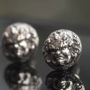 May include: A pair of silver earrings featuring a detailed design of a mythical creature's face.