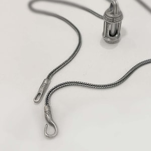 Peut inclure: Un collier en chaîne argent avec un pendentif argenté en forme de petite lanterne. Le pendentif porte l'inscription "The Dark".