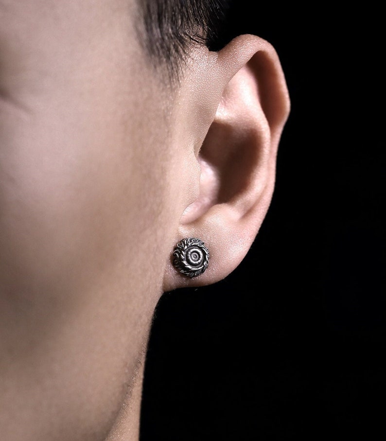 May include: A close-up of a person's ear with a silver earring featuring a detailed, circular design.