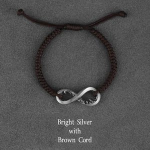 May include: A brown cord bracelet with a bright silver infinity symbol. The bracelet is adjustable and features a woven cord design. The text on the image reads "Bright Silver with Brown Cord."