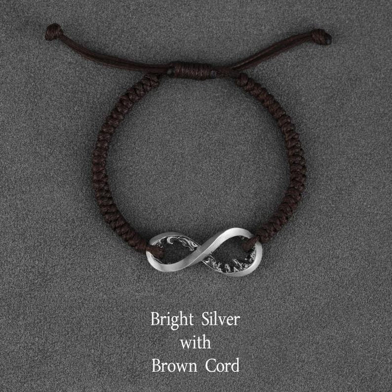 May include: A brown cord bracelet with a bright silver infinity symbol. The bracelet is adjustable and features a woven cord design. The text on the image reads "Bright Silver with Brown Cord."