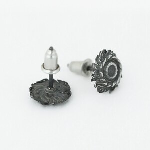 May include: A pair of silver stud earrings with a detailed design of a sun with rays. The earrings have a post and butterfly backing.