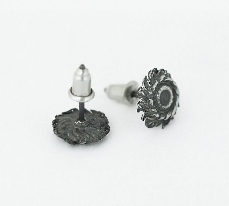 May include: A pair of silver stud earrings with a detailed design of a sun with rays. The earrings have a post and butterfly backing.