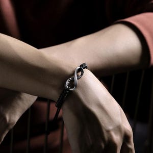 May include: Black braided bracelet featuring a silver infinity symbol. The bracelet has an adjustable cord closure. The infinity symbol is a prominent focal point, adding a touch of elegance to the accessory. The bracelet is designed for everyday wear.