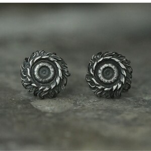 May include: A pair of silver earrings with a detailed, circular design resembling a stylized flower or sun. The center of each earring features a smaller circle.